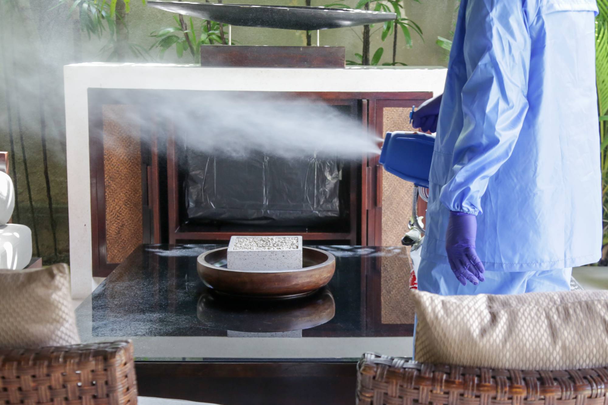 Eine Person in blauem Schutzanzug sprüht mit einem Gerät einen Nebel aus Desinfektionsmittel durch den Raum